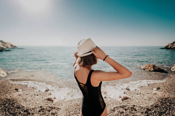 istock Young woman in hat standing on beach. rear view 968087154