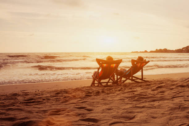 Tourism and travel vacation. Senior happy couple relaxing in luxurious resort sunset beach in deck chairs. Romantic honeymoon holidays. Recreation concept with copyspace. stock photo