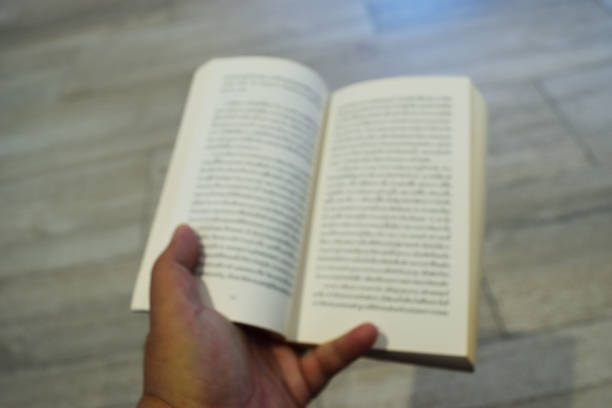 Accordion folded open miniature book with blank pages on the palm of the female hand against a wooden table background. Education and reading concept.