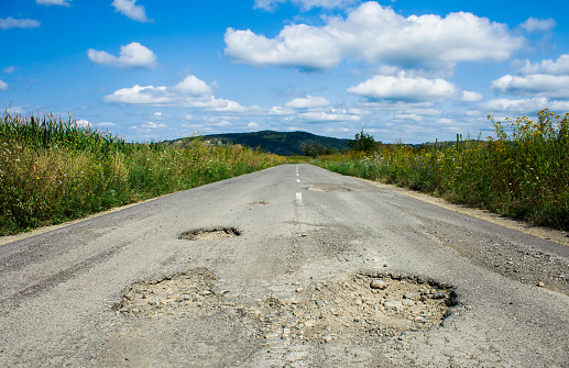 A great big pothole has formed in a road, created when the tarmac surface of the road has failed.