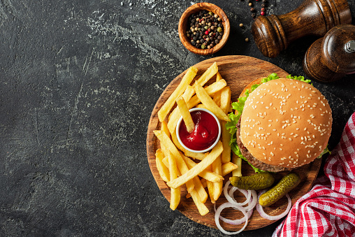 Burger and fries on wooden board on dark stone background. Homemade burger or cheeseburger, french fries and ketchup. Tasty sandwich. Top view with copy space for text