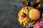 Burger and fries on wooden board on dark stone background