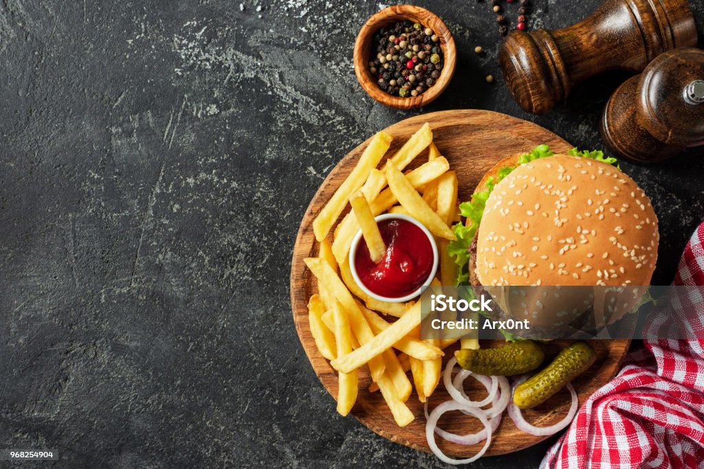 Burger and fries on wooden board on dark stone background Burger and fries on wooden board on dark stone background. Homemade burger or cheeseburger, french fries and ketchup. Tasty sandwich. Top view with copy space for text Burger Stock Photo