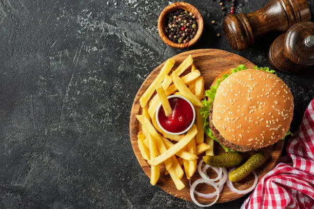 Photo of Burger and fries on wooden board on dark stone background