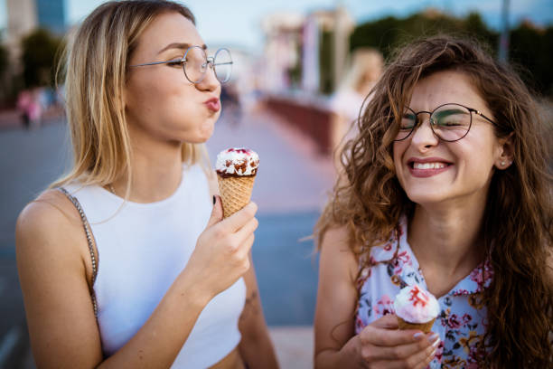 Beautiful women eating ice cream in walk Two smiled women eating ice cream while walking during sunny summer day. making a face stock pictures, royalty-free photos & images