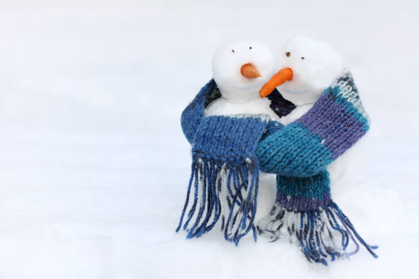 two smiling snowmen with carrot noses in a blue scarf on a background of a snowy landscape