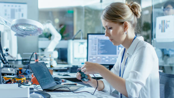 istock Female Computer Scientists Connects Circuit Board to Her Laptop and Starts Programming it. She Works in the Technologically Advanced Laboratory. 968289522