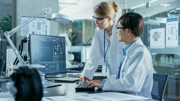istock Asian Scientist Sitting at His Desk Consults Senior Engineer about Sophisticated Coding and Programming. In the Background Computer Science Research Laboratory with Robotic Arm Model. 968289644