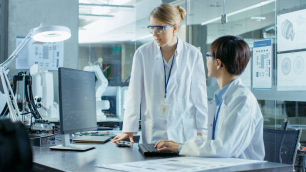 istock Asian Scientist Sitting at His Desk Consults Senior Engineer about Sophisticated Coding and Programming. In the Background Computer Science Research Laboratory with Robotic Arm Model. 968289650