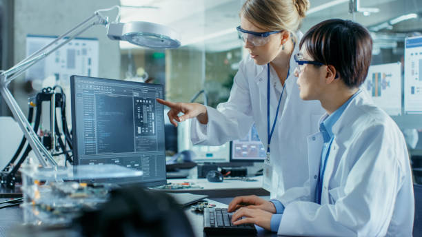 istock Asian Scientist Sitting at His Desk Consults Senior Engineer about Sophisticated Coding and Programming. In the Background Computer Science Research Laboratory with Robotic Arm Model. 968289652