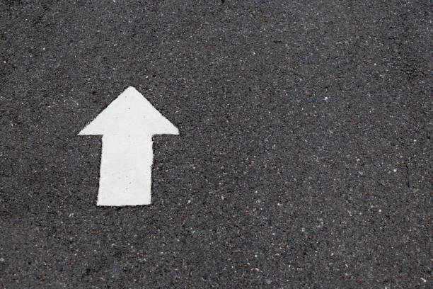 istock White painting in forward direction arrow symbol on black asphalt road background 968289922