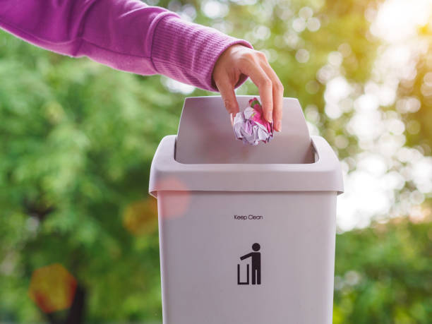 istock female hand trowing a paper into a garbage bin on bokeh background. cleaning concept. 968306164