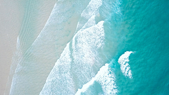 Turquoise blue ocean water white wash crashing on shoreline sand beach drone aerial from above