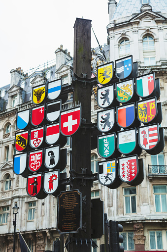 London, England - February 22, 2018: Swiss Court, part of Leicester Square in Central London. Leicester Square is at the heart of London’s entertainment district, with several cinemas and other places of interest. At the entrance of the court, there is a wooden post displaying with the 26 coat of arms of the Swiss Confederation and behind it, the Swiss glockenspiel.