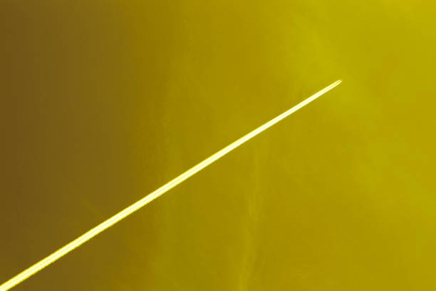 The plane flies high in the yellow sky and the white track from the airplane