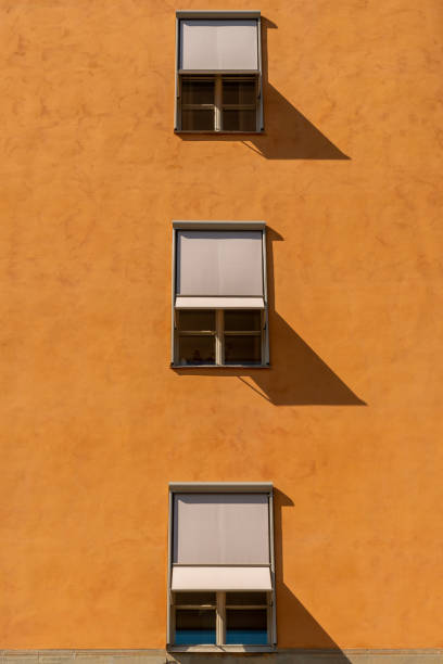 Front view of three symmetrical windows with sun blinds on a stone city building. Vertical composition.
