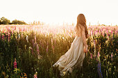 Young woman walking on flower field at sunset on background. Horizontal view with copy space