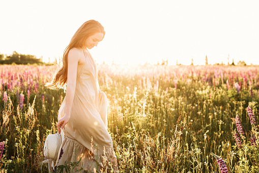 Joven mujer caminando en el campo de flores de lupino con salida del sol en el fondo. Luz cálido rayo de sol naranja photo