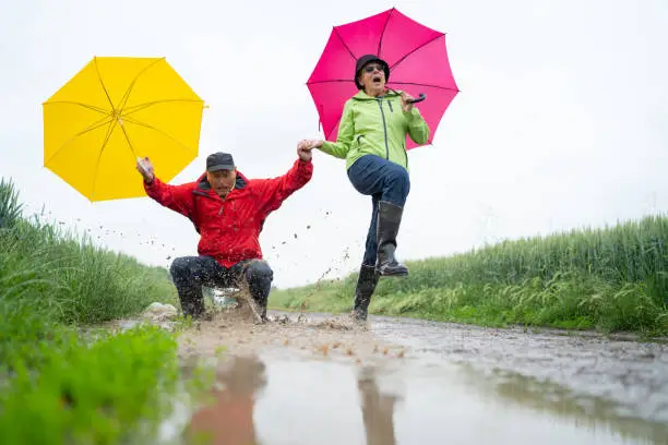 Photo of senior couple having fun on rainy day jumping in puddle
