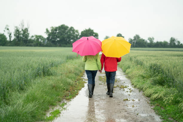 back view senior couple with umbrellas walking on rainy day