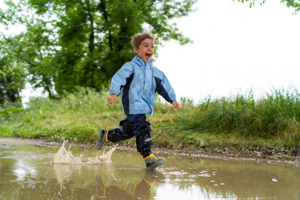 istock cheerful little boy in rain outfit running through puddle crying with open mouth 968397692