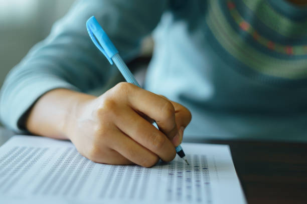 College student write on exam paper Close up of high school or university student holding a pen writing on answer sheet paper in the examination room. College students answering multiple choice questions test in the testing room in university. school test results stock pictures, royalty-free photos & images