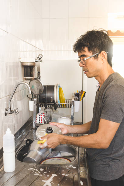 istock Asian man standing and washing dishes on a messy kitchen 968422482
