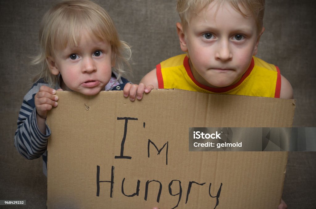 A hungry boy and a girl with a cardboard tablet with the inscription I'm hungry . Hungry Stock Photo