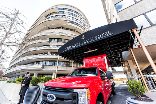 Washington DC, USA - April 5, 2018: Watergate hotel sign building in capital city, red truck, porter, doorman, security guard in winter coat and hat, residential building closeup