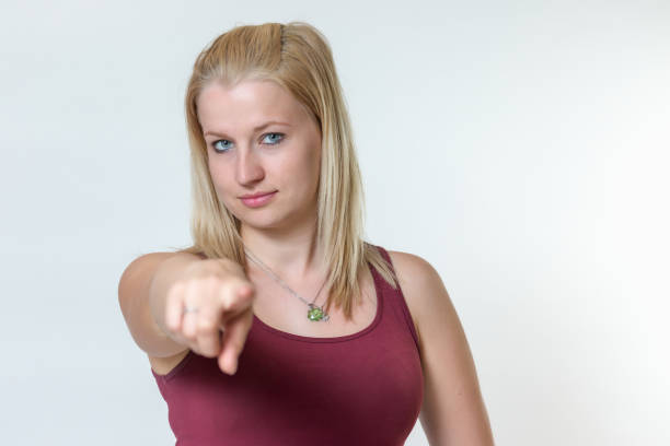 Studio shot of the attractive young blond woman in sportswearand seriously looking at the camera and finger pointing at the camera
