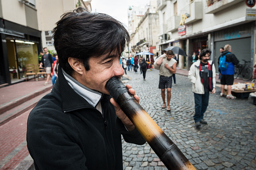 Buenos Aires, Argentina - February 05, 2017: Street performer is seen playing Didgeridoo in San Telmo, Buenos Aires neighborhood, capital Argentina. The didgeridoo (also known as a didjeridu) is a wind instrument developed by Indigenous Australians.