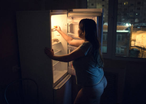 Sexy chubby woman craving and looking for food in a frige late at night. Girl dressed in homewear t-shirt and panties. Authentic atmosphere of the kitchen stock photo
