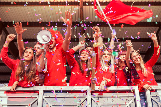 group of fans dressed in red color watching a sports event stock photo