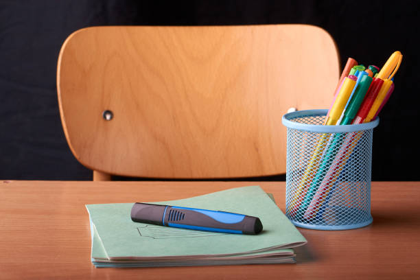 Colored Pens in a blue metal basket on desk in school on black background