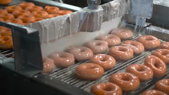 fresh donuts being glazed by machine in donut factory assembly line