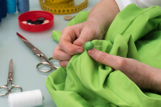 istock Seamstress sews the button to a green shirt 968517424