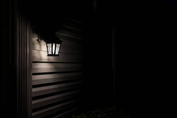Dark night evening with house exterior lamp lantern, illuminated front door porch with black background on wall siding