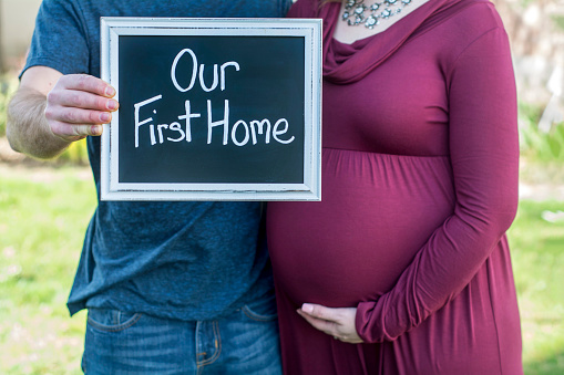 new homeowners hold up sign for their first new buy and excitement of new life stage while pregnant