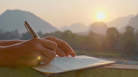 Mujer joven escribiendo páginas de mañana en diario al aire libre, primer plano photo