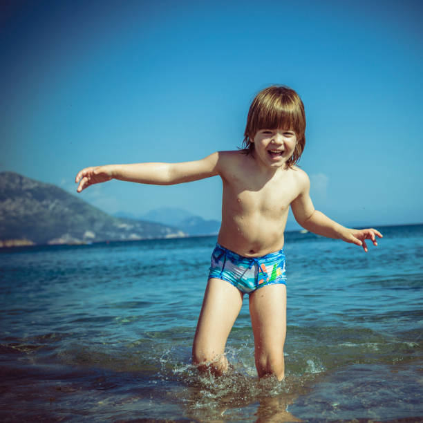 Little cheerful boy running in sea water during perfect sunny summer day at the beach. Spontaneous, old styled photo.