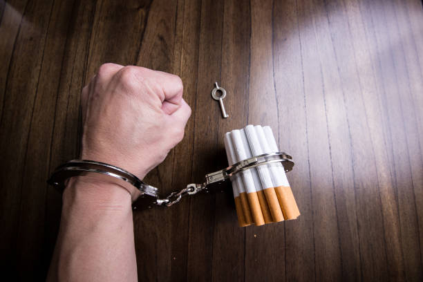 Concept of handcuffs with hand and cigarettes on other end Concept of handcuffs with hand and cigarettes on other end gun laws stock pictures, royalty-free photos & images