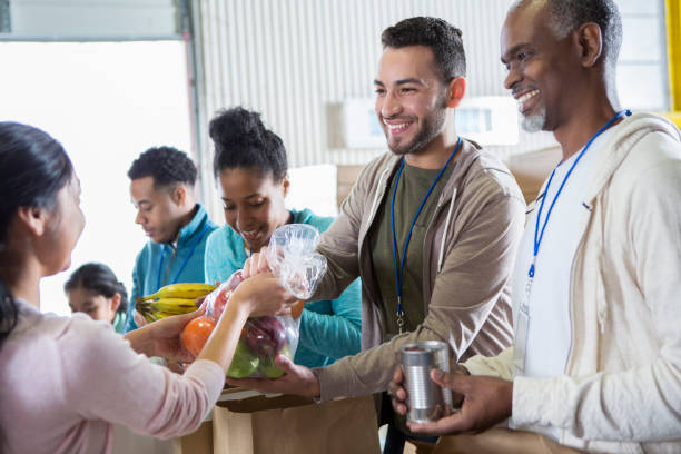 Cheerful volunteers receive donations during food drive Male friends volunteer together at a food bank. They are receiving donated food items. non profit organization photos stock pictures, royalty-free photos & images