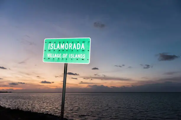 Sunrise in Islamorada, Florida Keys, with orange blue sky, beach, green sign closeup, village of islands, in Atlantic Ocean, gulf of Mexico, horizon