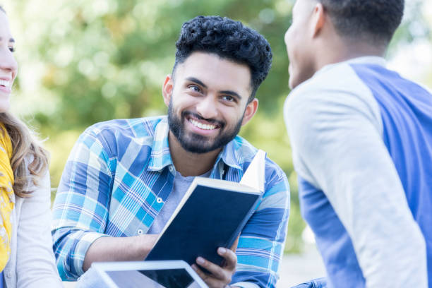 istock Happy college student reads book with friends 968606368