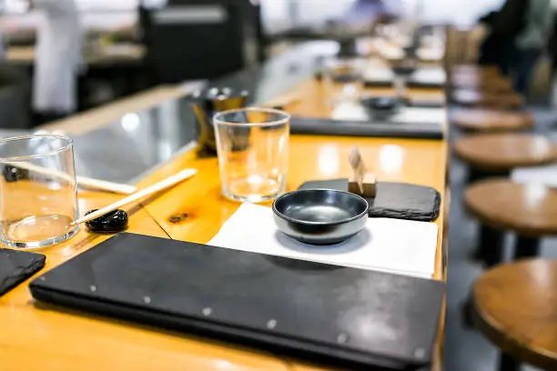 Japanese restaurant in traditional style, interior asian sushi wooden bar counter, menu, bowl, glass, napkin setting empty nobody closeup