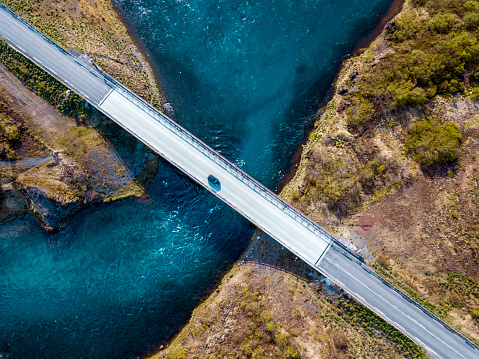 Aerial shoot of a car driving over bridge with fresh blue water running under.  Salmon river Sogid in Grimsnes south of Iceland can be seen from air.