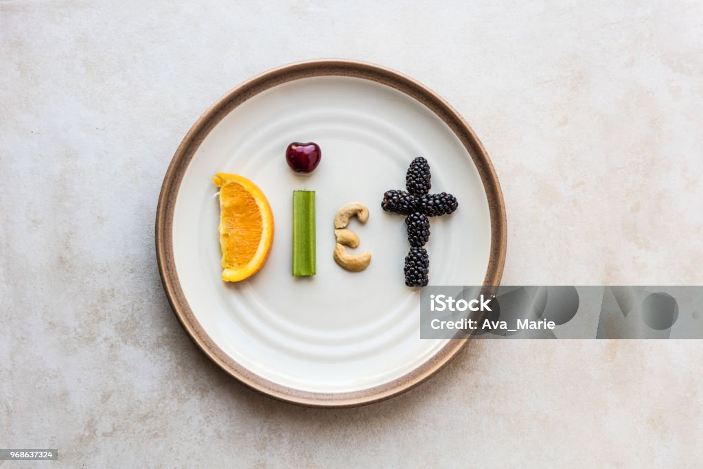Diet food fun on a plate The word Diet made from food. A orange slice, celery stick, cherry, cashew, and blackberry spell diet, as it sits on a stoneware plate. Using a flat lay over head view to capture the spelled out food word. Dieting Stock Photo