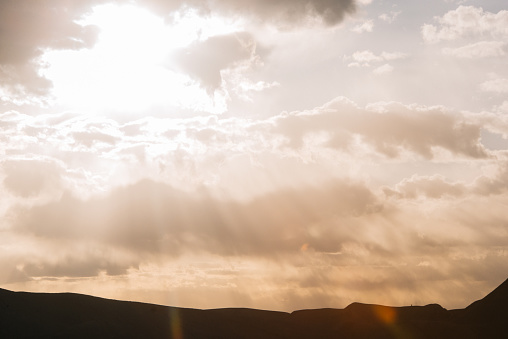 This is a color photograph of the morning sun shining through the cloudy sky over silhouetted mountains in Capitol Reef National Park, Utah.