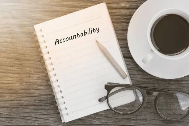 Photo of Accountability concept on notebook with glasses, pencil and coffee cup on wooden table. Business concept.