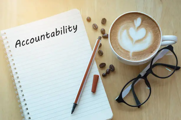 Photo of Accountability concept on notebook with glasses, pencil and coffee cup on wooden table. Business concept.